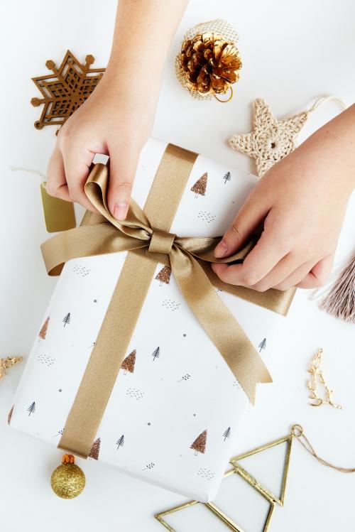 Woman tying a gold ribbon to a white present - 1231767