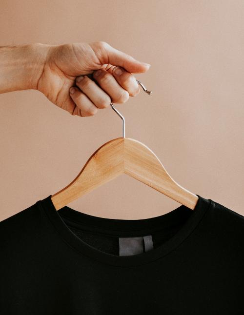 Hands holding a black t-shirt in a hanger - 1235328