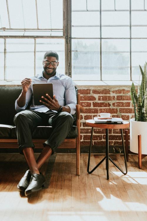 Cheerful black man using a stylus with a digital tablet in a living room - 1219055