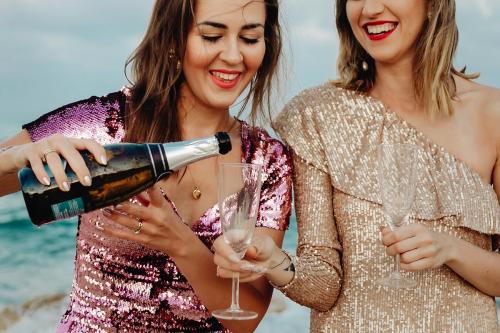 Women filling up a glass of champagne at the beach - 1228540