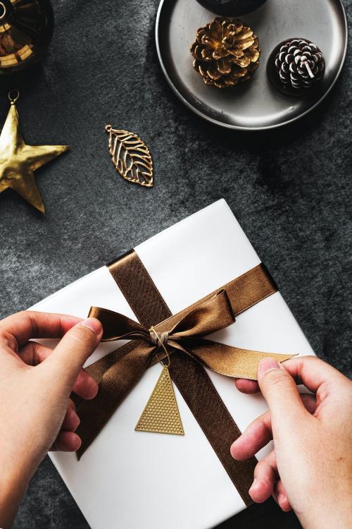 Woman tying a golden brown ribbon to a present - 1231751