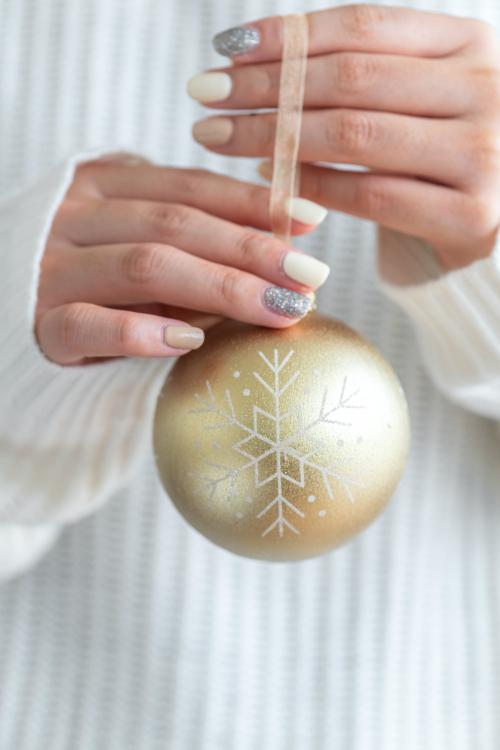 Woman in a white sweater holding a gold bauble - 1231893