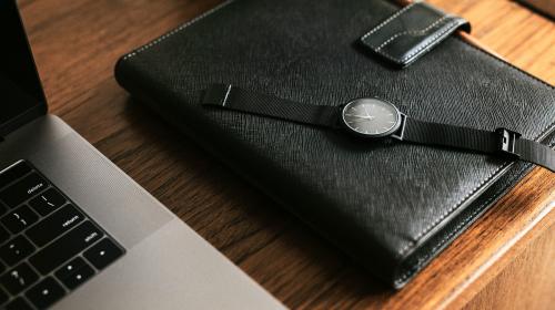 Black planner on a wooden desk by a laptop - 1224510