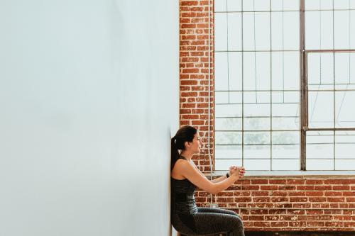 Sporty woman doing squats against a wall - 1225150