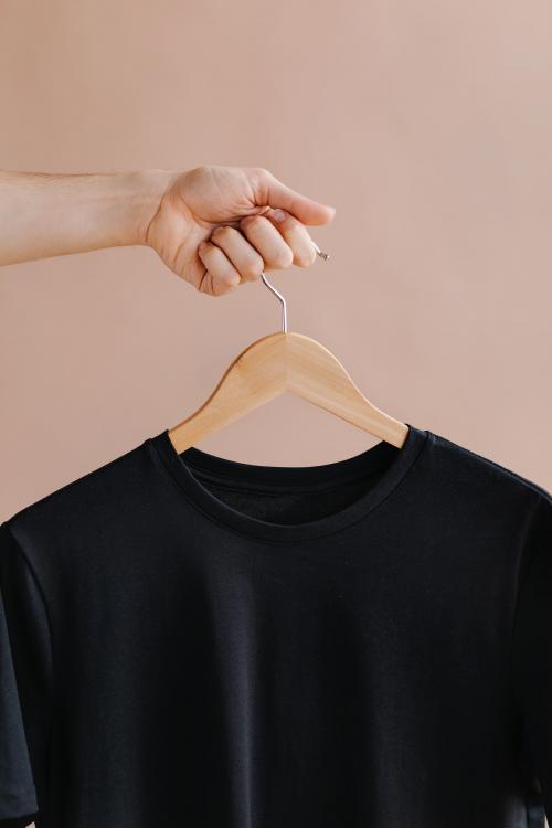 Hands holding a black t-shirt in a hanger - 1235371