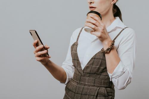 Businesswoman drinking coffee while checking her phone - 2020052