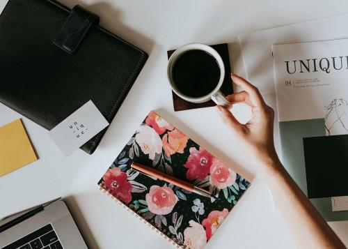 Woman holding her coffee by a floral book - 1220787