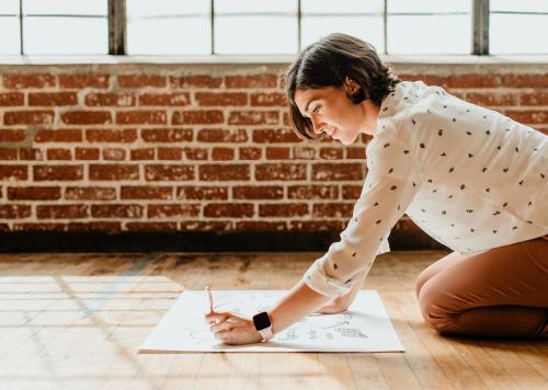 Happy woman writing on a white chart paper on the floor - 1226536