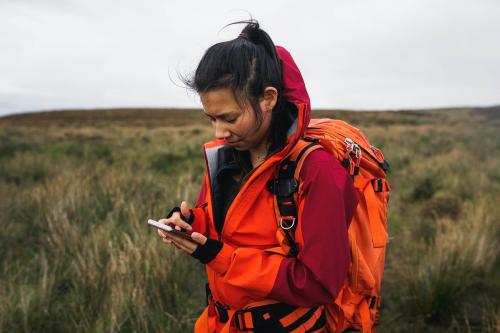 Female hiker using her phone in a grass field - 1233376