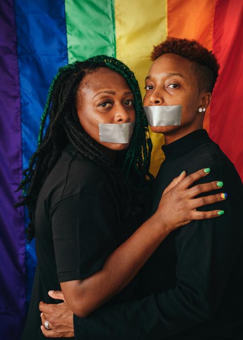 Lesbian couple wearing tapes on their mouth against a rainbow background - 1205430