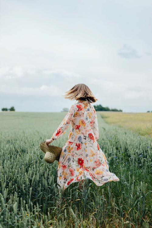 Woman in a floral dress with a woven hat in a field - 1207957