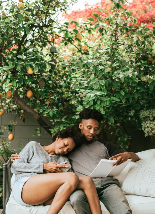 Black couple reading and playing on the phone in the garden - 1211717