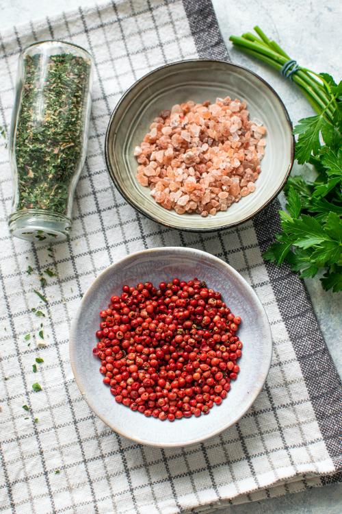 Pink pepper in a bowl next to a cup of Himalayan salt flatlay - 1215728