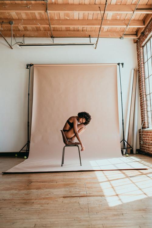 Black woman curling up on a chair in a studio - 1218986