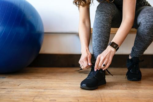 Active woman wearing a smartwatch tying her shoelaces - 1225112