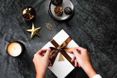 Woman tying a golden brown ribbon to a present - 1231795