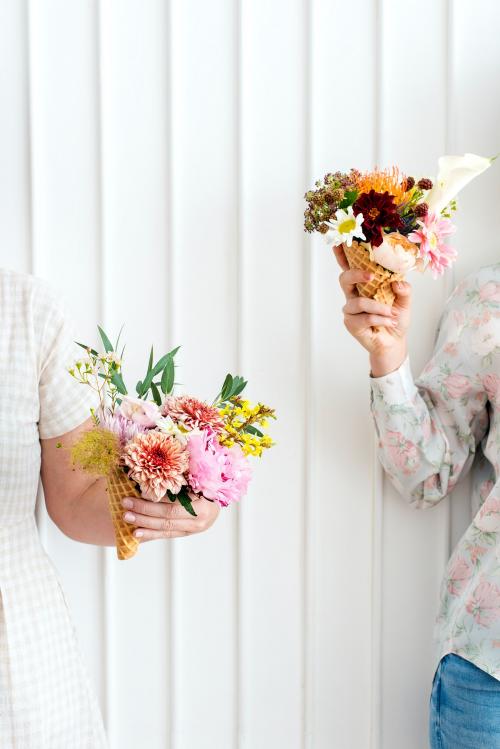 Two women holding up flowers in ice cream cones - 1207378