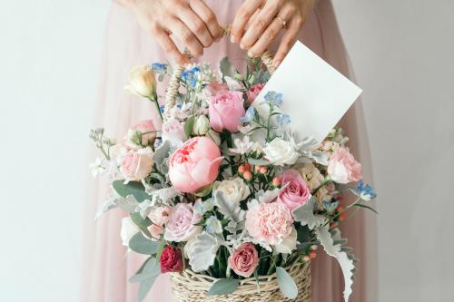 Hand carrying a basket filled with assorted colorful flowers and a note card - 1207536