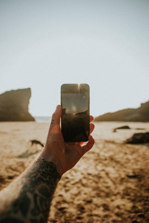 Tattooed man using a mobile phone camera on the beach - 1215651