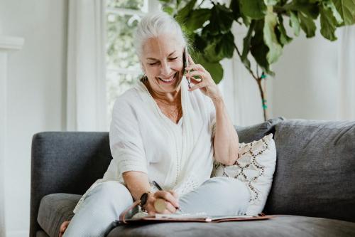 Cheerful elderly woman talking on a phone on a couch - 1211851