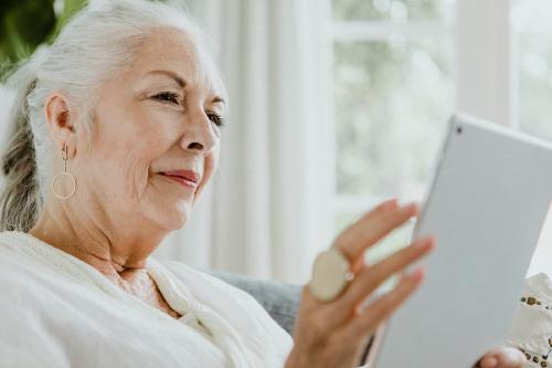 Elderly woman using a tablet on a couch - 1211855