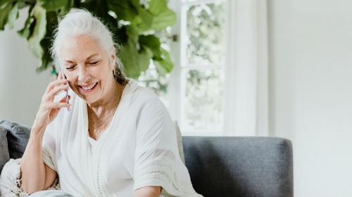 Cheerful elderly woman talking on a phone on a couch - 1211873