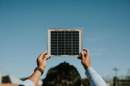 Rearview of eco-friendly woman holding a solar panel up in the sky - 1213884