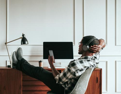 Black man with headphones playing on his phone sitting at his desk - 1209094