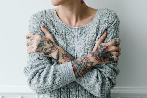 Tattooed woman in a gray sweater hugging herself - 1212508