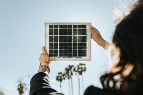 Rearview of eco-friendly woman holding a solar panel up in the sky - 1213910