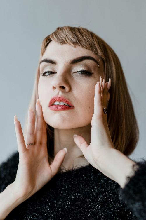 Brown hair woman in a black fluffy sweater touching her cheeks - 1216418