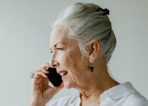 Cheerful senior woman talking on a phone in a white room - 1201690