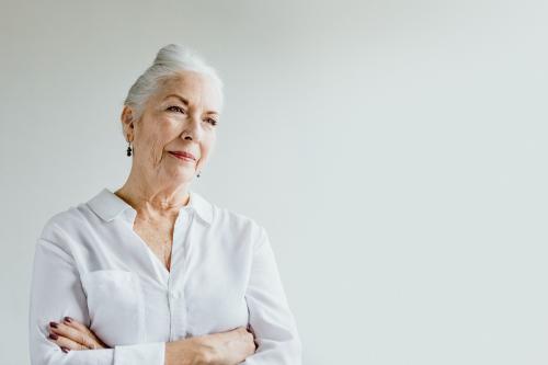 Cheerful crossed arms senior woman by the window in a white room in a white room - 1201697