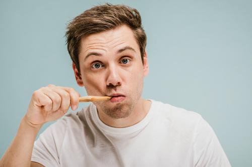 Blond man brushing his teeth with a wooden toothbrush - 1203217