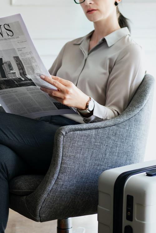 Businesswoman with a suitcase reading a newspaper - 1208699