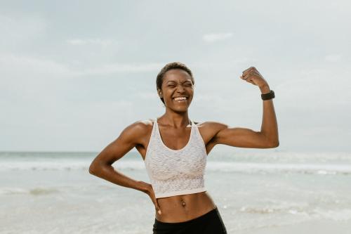 Cheerful black woman flexing her muscles by the seaside - 1079815