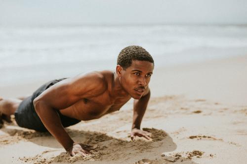 Muscular black man doing pushups at the beach - 1079933