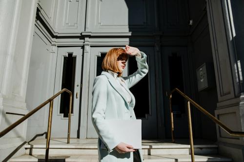 Woman in an overcoat carrying a white box in front of a building - 1198648