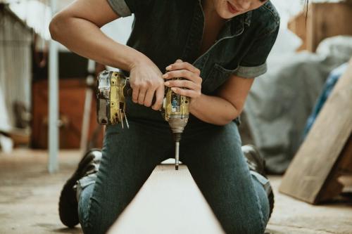 Female carpenter drilling a lumber - 1199242