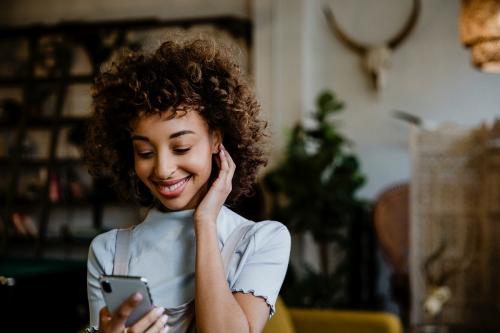 Cheerful black woman using her phone in living room - 1200587