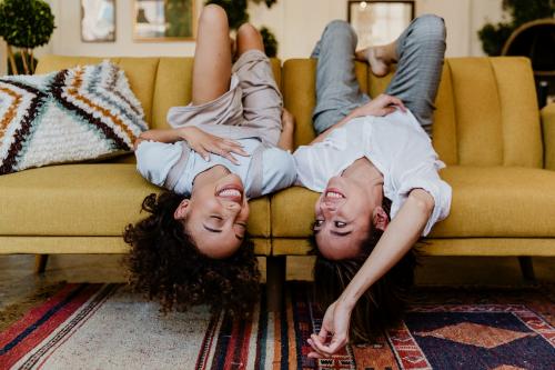 Cheerful women lying upside down on a mustard yellow couch - 1200613