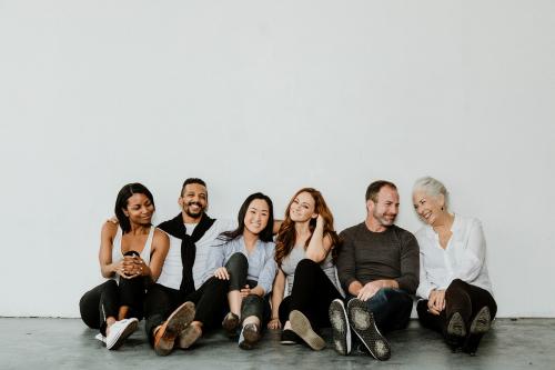 Group of cheerful diverse people sitting on a floor in a white room - 1201617