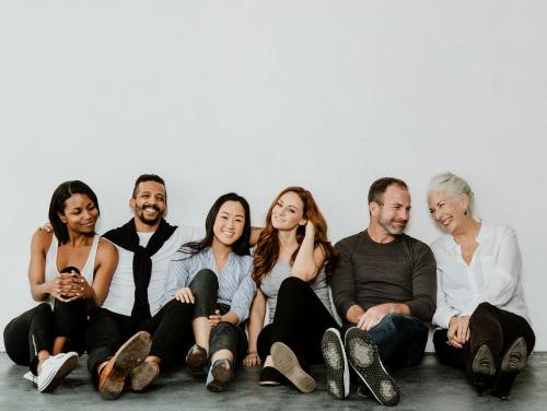 Group of cheerful diverse people sitting on a floor in a white room - 1201711