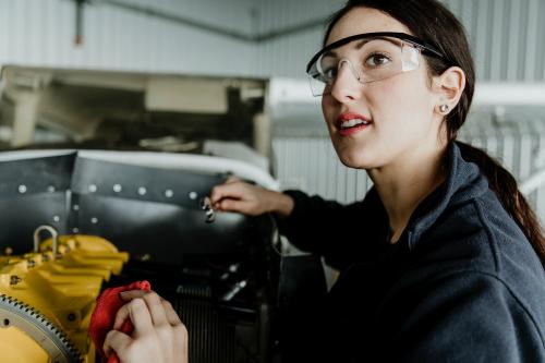 Female aviation technician repairing the motor of a propeller plane - 1202217