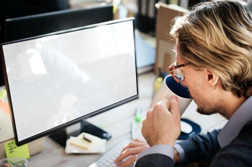 Caucasian man drinking a coffee whilst using a desktop with design space - 5323