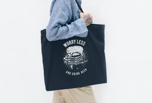 Tattooed woman in a blue linen shirt holding a black tote bag mockup - 1215330