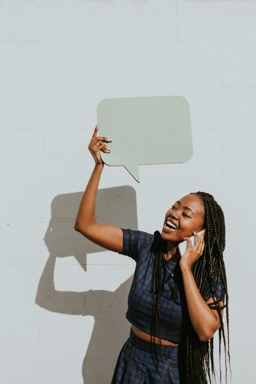 Cheerful black woman showing a blank speech bubble while talking on a phone - 1208479