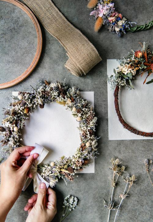 Woman tying a ribbon on a floral wreath over a white card mockup - 1209992