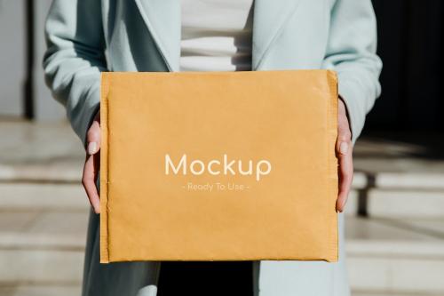 Woman holding a brown envelope mockup in front of a building - 1198717