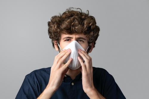 Young man wearing a pollution mask standing by a gray wall mockup - 2209625